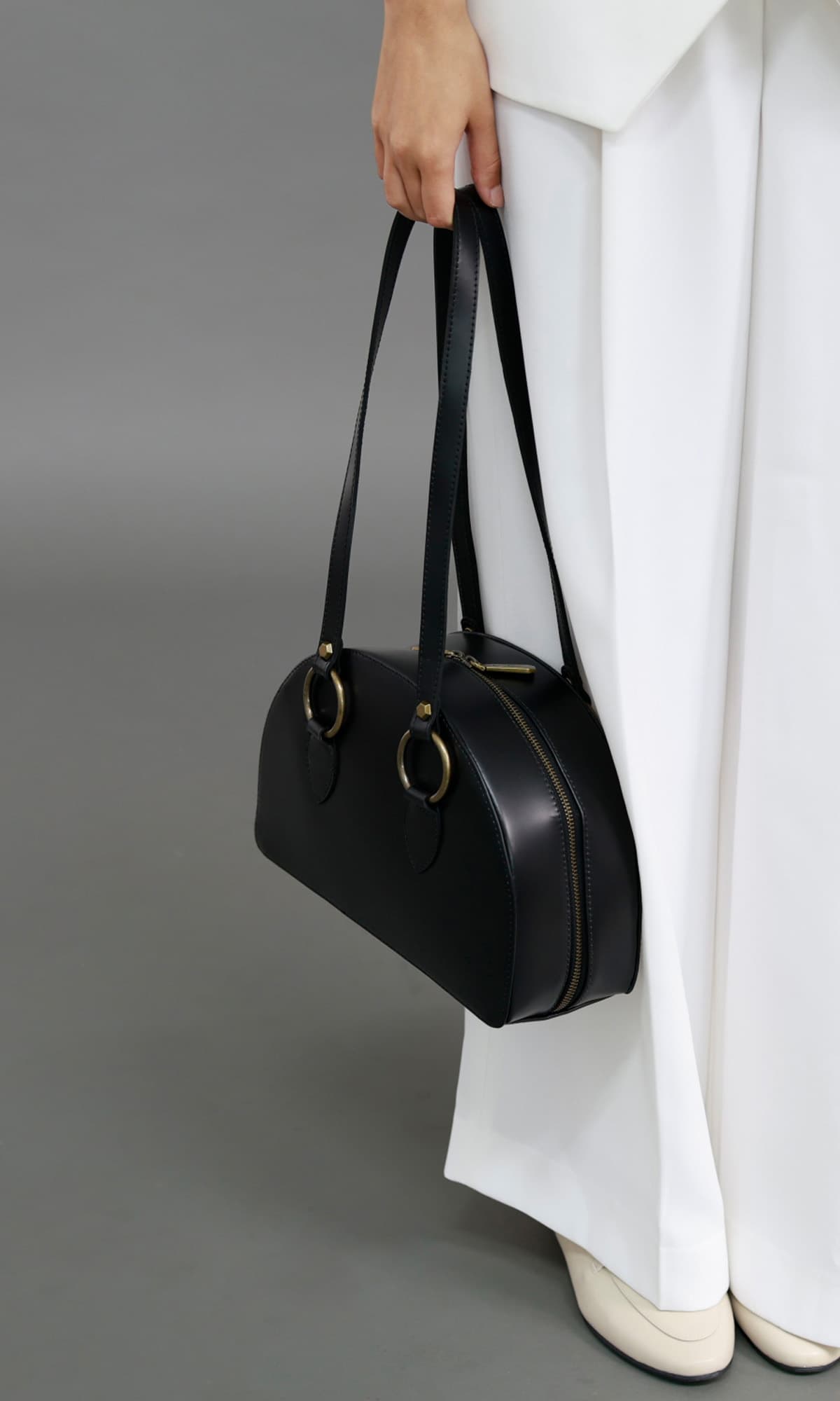 Rebecca Retro Bowling Bag in black leather — model holding the bag by the top handles, showing scale, structured shape and smooth leather finish